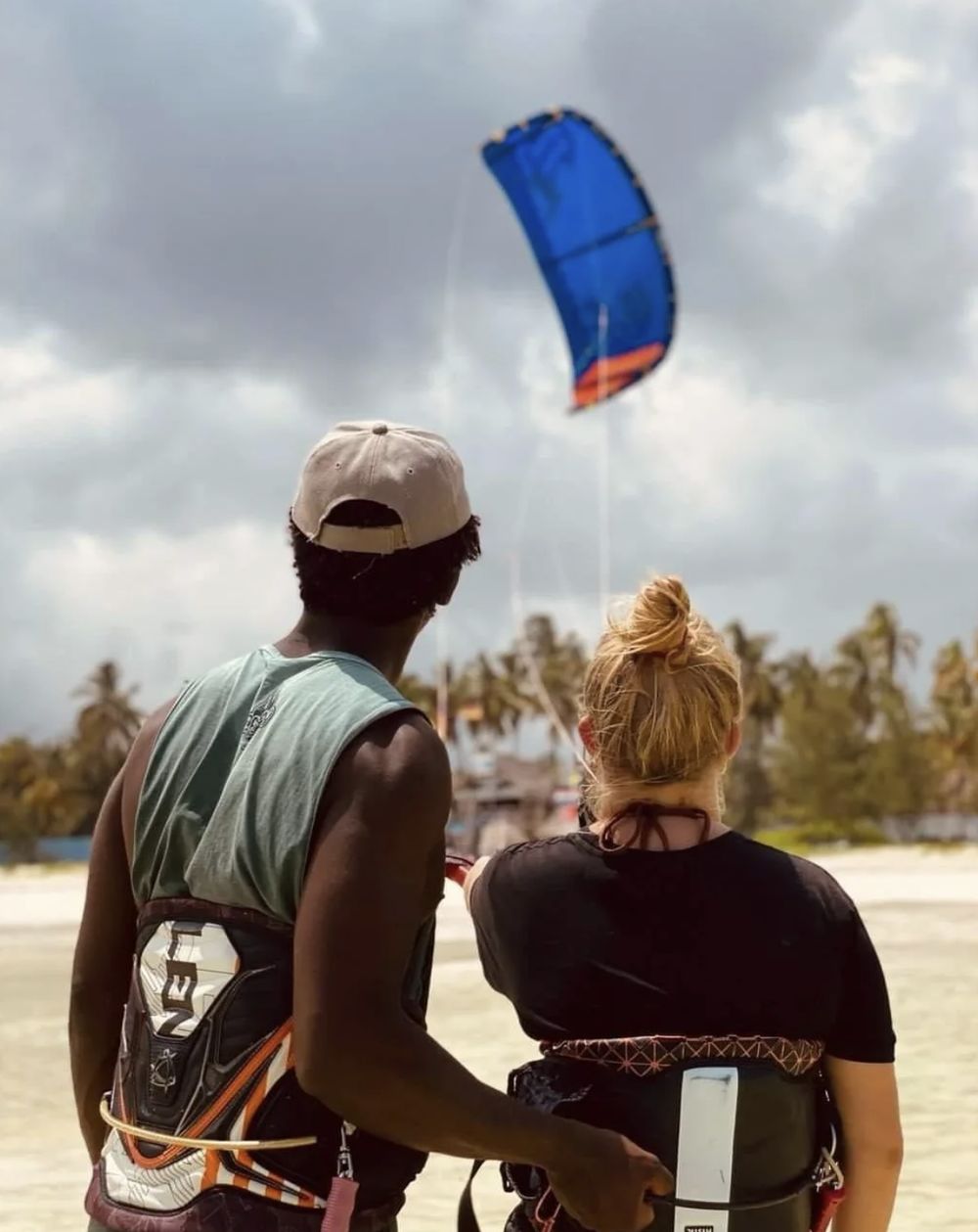 An instructor and a student on the beach in Paje, watching a blue kite in the sky