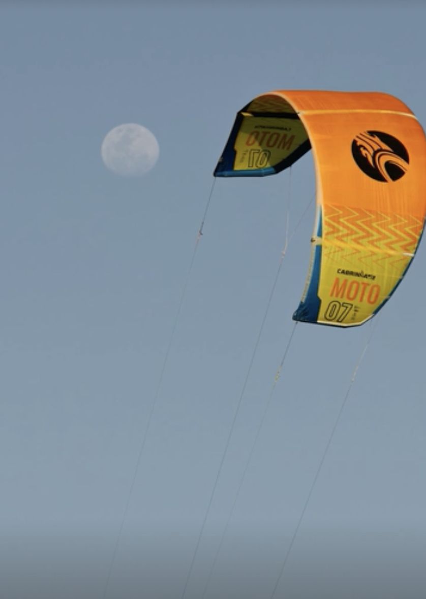 An orange kite in a clear sky with the moon beside it
