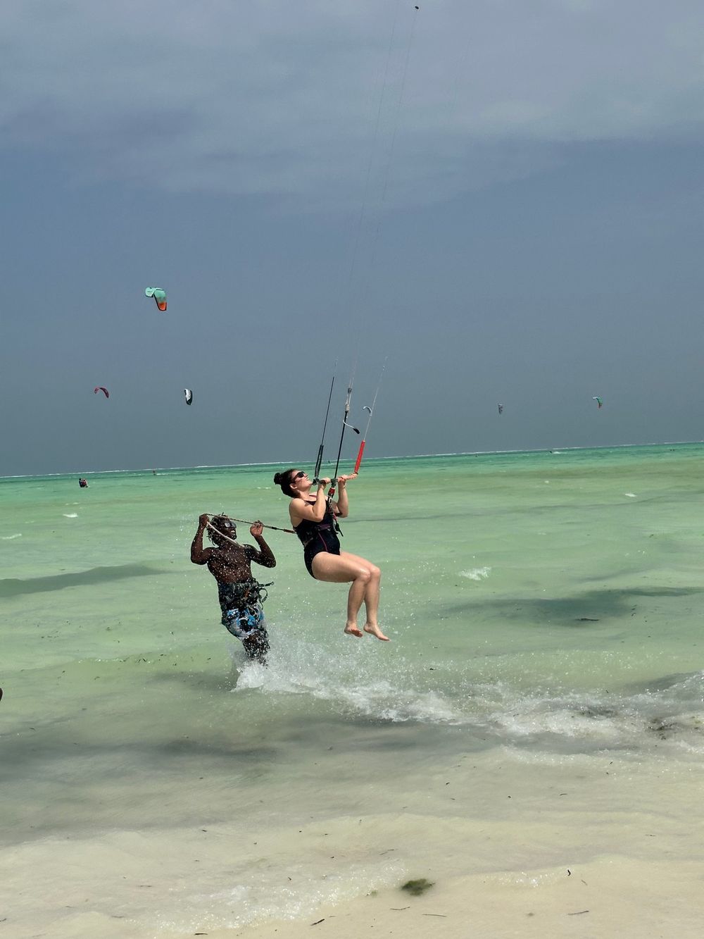 An instructor walking through shallow turquoise water while a student flies the kite